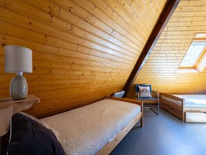 Ein kleiner Raum mit Holzwänden, einem Bett, einem Stuhl und einem Tisch mit einer Lampe.