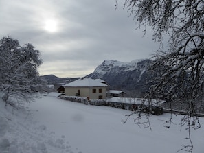 A snow-covered house with a mountain backdrop. - Apartment with parking, pets welcome - 8 guests (Arâches-la-Frasse)