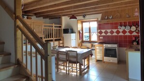 A rustic kitchen with wooden beams, a dining table with chairs, a window with a view, and a stove. - Apartment with parking, pets welcome - 8 guests (Arâches-la-Frasse)