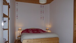 A bedroom with a wooden bed, two bedside lamps, a ladder, and a hanging star decoration. - Apartment with parking, pets welcome - 8 guests (Arâches-la-Frasse)