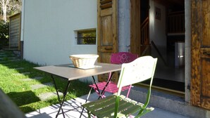 A patio with a table and chairs, a basket, and a wooden door leading to an interior staircase. - Apartment with parking, pets welcome - 8 guests (Arâches-la-Frasse)