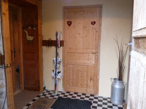 Eine Holztür mit herzförmigen Verzierungen, ein Kleiderständer mit Ski und ein Schachbrettfußboden.