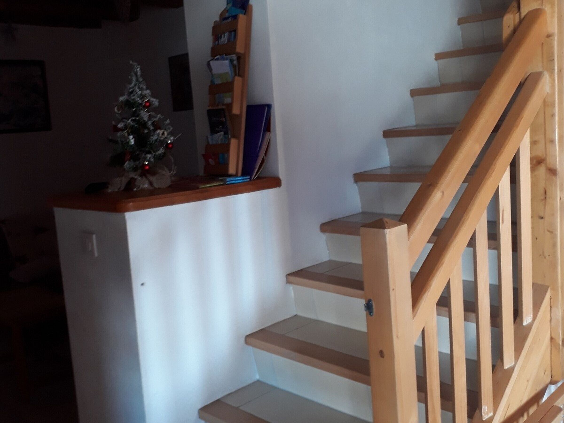 Eine Treppe mit Holhandläufen und eine kleine Weihnachtstanne an einer weißen Wand.