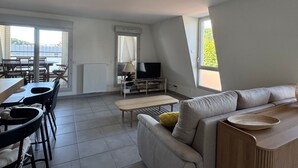 A modern living room with a sofa, a TV, a dining area with chairs and a table, and large windows. - Bright apartment with mountain view - 4 guests (Aix-les-Bains)