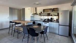 A modern kitchen with a dining area, featuring a central island, chairs, a refrigerator, and built-in shelves. - Bright apartment with mountain view - 4 guests (Aix-les-Bains)