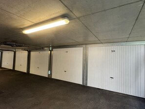 Eine Tiefgarage mit weißen, nummerierten Schließfächern von 12 bis 20, Neonbeleuchtung und Betonböden.