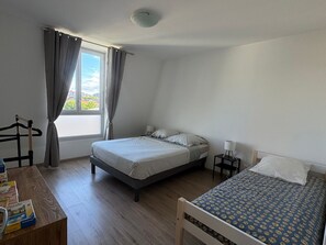 Een slaapkamer met een bed, een bijzetbed, een nachtkastje, een lamp, een houten stoel en een raam met gordijnen.