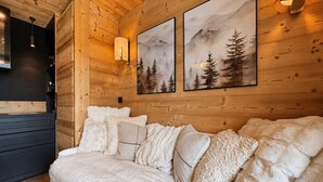 Une chambre confortable dans un chalet en rondins, avec un lit, une lampe fixée au mur et deux tableaux encadrés représentant des paysages de montagne.
