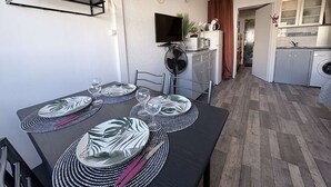 Ruokailutila, jossa on neljälle katettu ruokapöytä, televisio ja taustalla näkyvä keittiö.