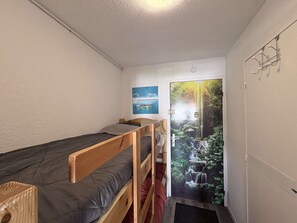 A small, single-room accommodation with a bunk bed, a door with a forest mural, a small table, and a wall-mounted light fixture. - Apartment in Gruissan, ideal location (Gruissan)