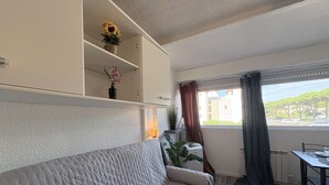 Moderni olohuone, jossa on sohva, ruokapöytä, ikkuna verhoilla ja hyllyllä oleva kasvi.