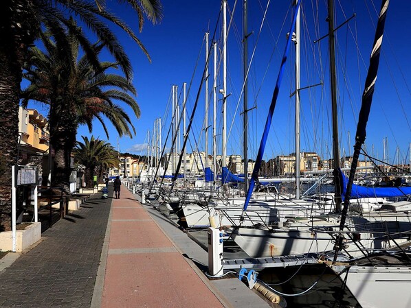 A marina with multiple boats docked, a pedestrian walkway, and palm trees. - Apartment in Gruissan, ideal location (Gruissan)