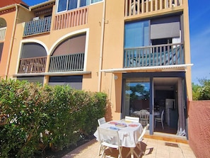 A two-story building with balconies, a covered patio with a table and chairs, and a sliding glass door entrance. - Studio with pool and parking - 4 guests (Canet-en-Roussillon)