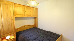 A bedroom with a wooden bed frame, a dark quilted bedspread, and a hanging light fixture. - Apartment with mountain view - 4 guests (Bagnères-de-Luchon)