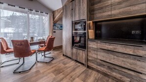 Moderni keittiö, jossa on puiset kaapit, sisäänrakennettu uuni ja ruokailutila tuoleineen.
