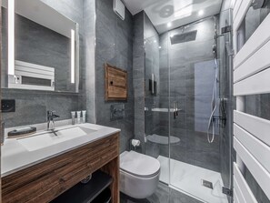 Une salle de bain moderne avec un grand miroir, un meuble-lavabo en bois, des toilettes et une douche séparée par une paroi de verre.