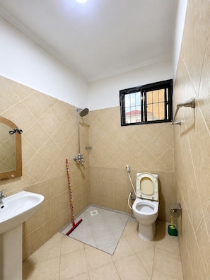 Een badkamer met toilet, wastafel, douche en een raam met tralies.