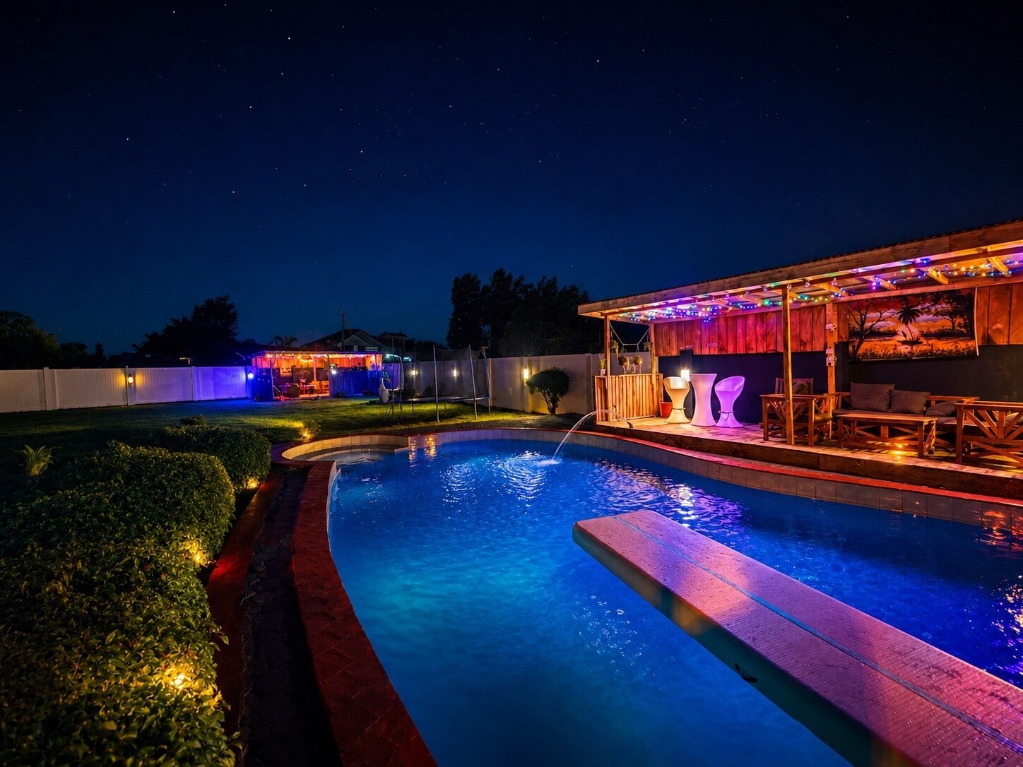 A swimming pool with a wooden deck and a covered seating area with string lights.