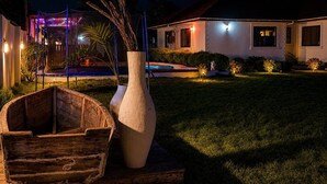A house with a swimming pool, a wooden boat, and a large vase with plants.