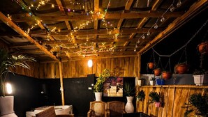 A rustic wooden room with wicker furniture, hanging plants, and string lights.