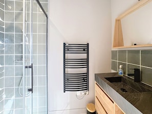 Ein modernes Badezimmer mit Duschkabine aus Glas, einem schwarzen Handtuchhalter, einem Holzkosmetikschrank mit dunkler Arbeitsplatte und einem Spiegel über dem Waschbecken.