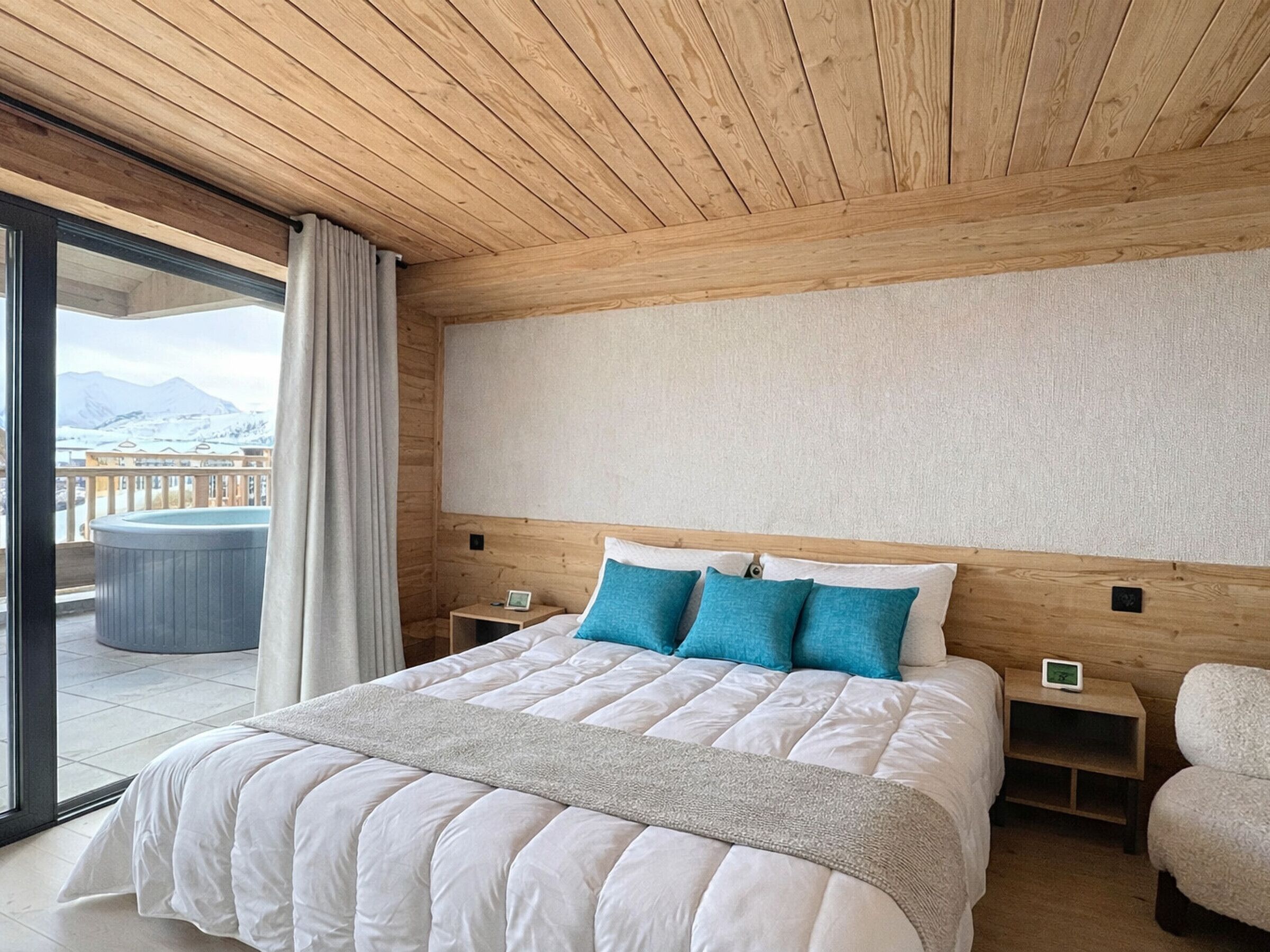 A bedroom with a large bed, wooden ceiling, and a view of mountains through a glass door.