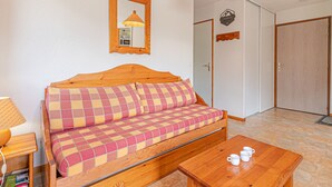 Ett rum med en soffa i trä, ett träbord med muggar, en lampa och en spegel på väggen.