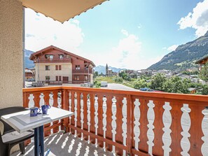 Un balcon avec une table et des chaises, donnant sur une ville, avec des bâtiments et des montagnes en arrière-plan.