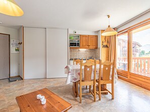 Eine Küche mit Holzausstattung, einem Esstisch mit Stühlen und Blick auf Berge vom Balkon.