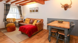 Una habitación acogedora con techo de madera, un sofá de cuero marrón, una manta roja, una mesa de comedor con sillas y una decoración de cabeza de toro montada en la pared.