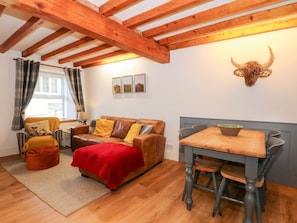 Una habitación acogedora con techo de madera, un sofá de cuero marrón, una manta roja, una mesa de comedor con sillas y una decoración de cabeza de toro montada en la pared.
