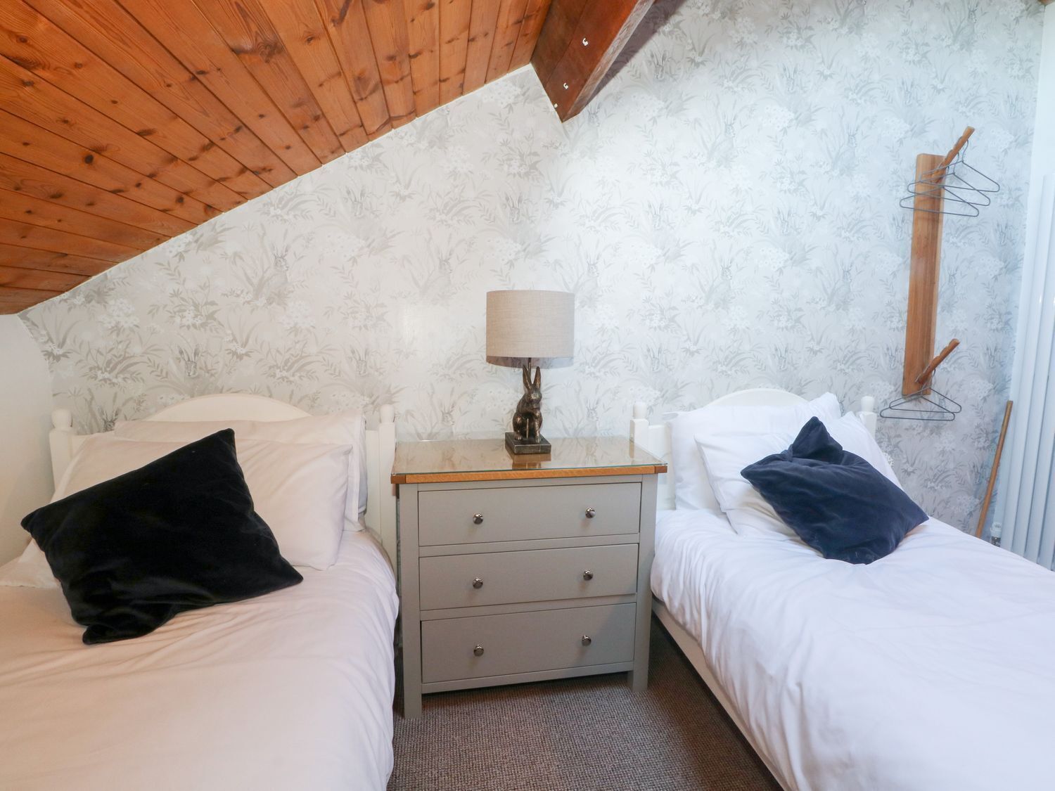 Un dormitorio con dos camas, una mesita de noche con lámpara y techo de madera.