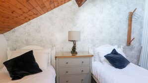 Un dormitorio con dos camas, una mesita de noche con lámpara y techo de madera.