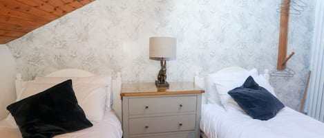 Quarto com duas camas, uma mesa de cabeceira com abajur e teto de madeira.