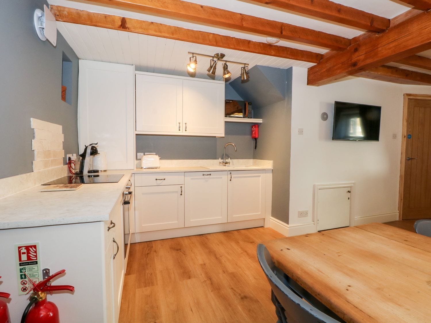Eine Küche mit weißen Schränken, Holzbalkendecke, Spüle, Toaster und Feuerlöscher.