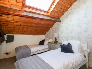 A bedroom with two beds, a skylight, wooden ceiling, and a patterned wallpaper. - Angels Nook (Settle)
