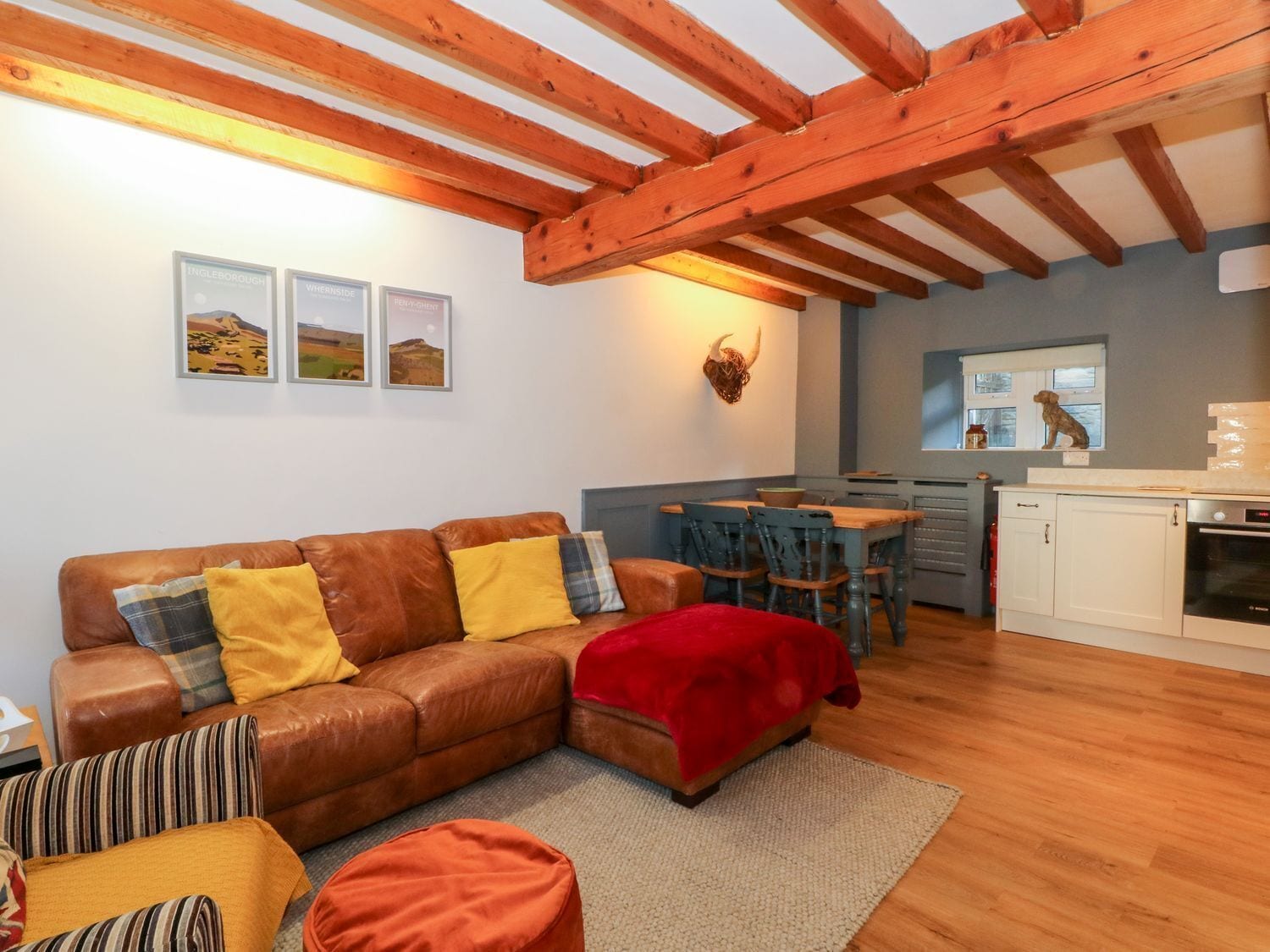 Uma sala de estar aconchegante com um sofá de couro marrom, um cobertor vermelho e uma área de jantar com mesa e cadeiras de madeira.