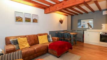 Uma sala de estar aconchegante com um sofá de couro marrom, um cobertor vermelho e uma área de jantar com mesa e cadeiras de madeira.