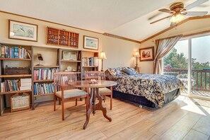 A bedroom with a bed, a dining table with chairs, a ceiling fan, and a balcony with a grill.