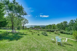 A grassy outdoor area with picnic tables and chairs, a large tree, and a view of a body of water and distant landscape. - CABIN - Pet Friendly, Lake View, Patio & Deck, Trails (Cokato)