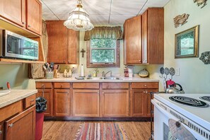 A kitchen with wooden cabinets, a microwave, a stove, and a window with a view of trees.