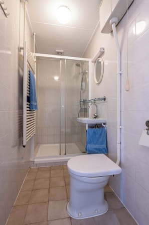 Un baño con inodoro, cabina de ducha, lavabo y toallero.