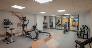 Un gimnasio con máquinas de cardio, equipo de levantamiento de pesas y un espejo grande.
