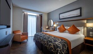 Une chambre d’hôtel avec un grand lit, une chaise, un bureau et une fenêtre avec des rideaux.