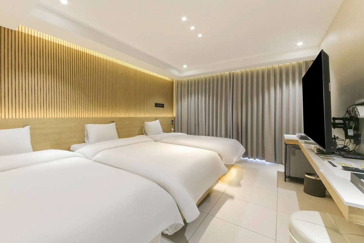Ein Hotelzimmer mit drei Betten, einem Schreibtisch mit Computer und einem Fernseher.