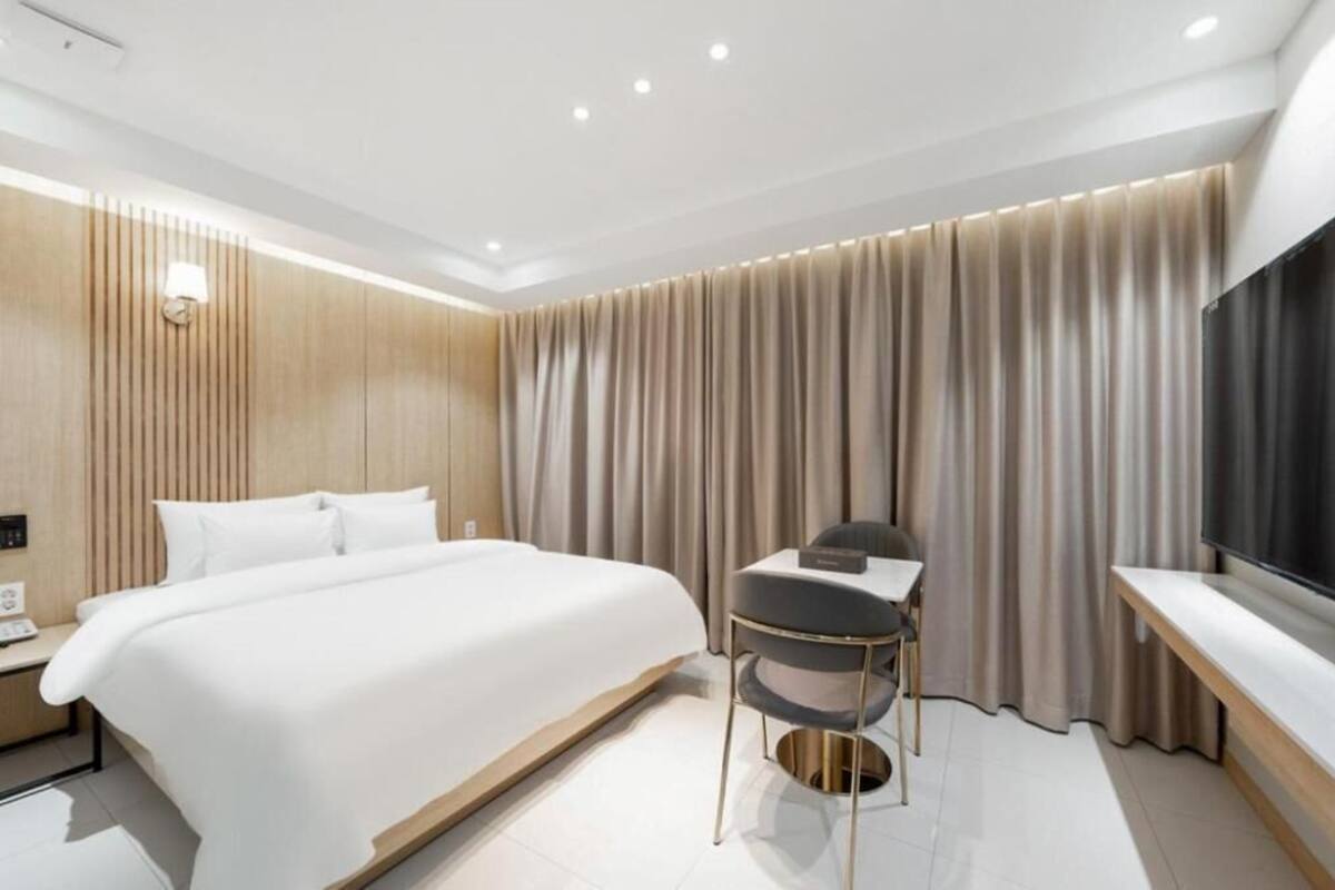 Ein modernes Hotelzimmer mit einem großen Bett, einem Schreibtisch mit Stuhl, einem Flachbildfernseher und einem großen Fenster mit Vorhängen.