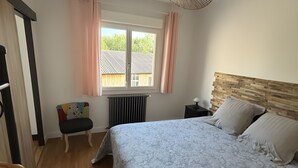 Une chambre à coucher avec un lit, une fenêtre avec des rideaux, un radiateur, une chaise et un ventilateur de plafond.