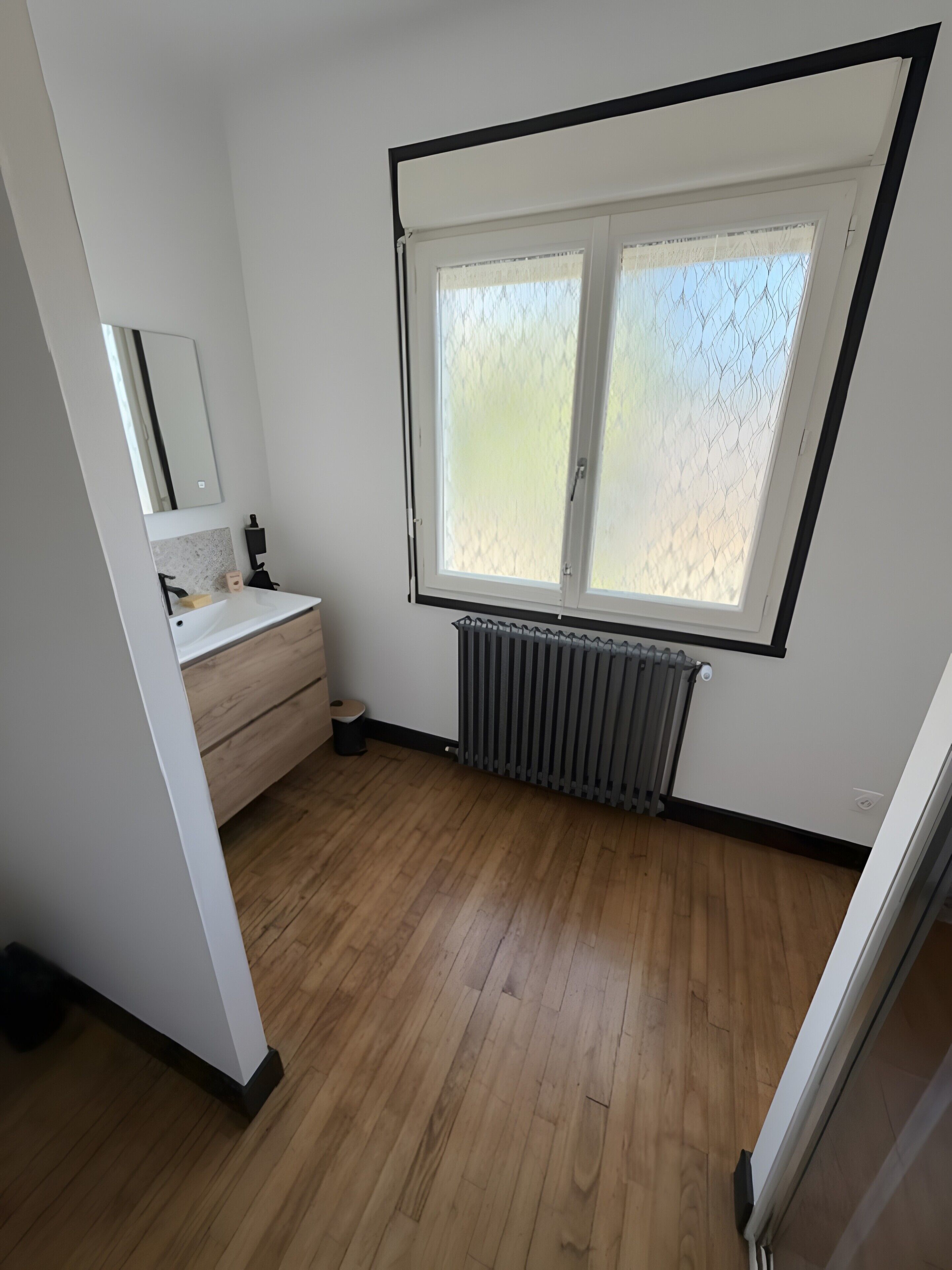 Une salle de bain avec un lavabo blanc, un miroir et une fenêtre.