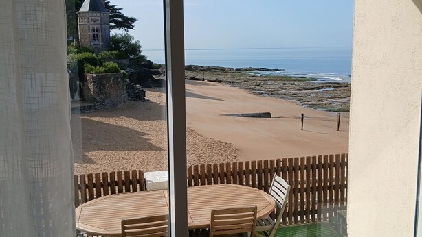 Ein Balkon mit Tisch und Stühlen, der Blick auf einen Strand und einen historischen Turm bietet.