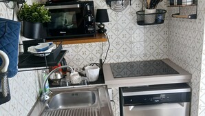 Eine kompakte Küche mit Spüle aus Edelstahl, einer Mikrowelle, einem Geschirrspüler und einer kleinen Ablage mit Küchenutensilien.